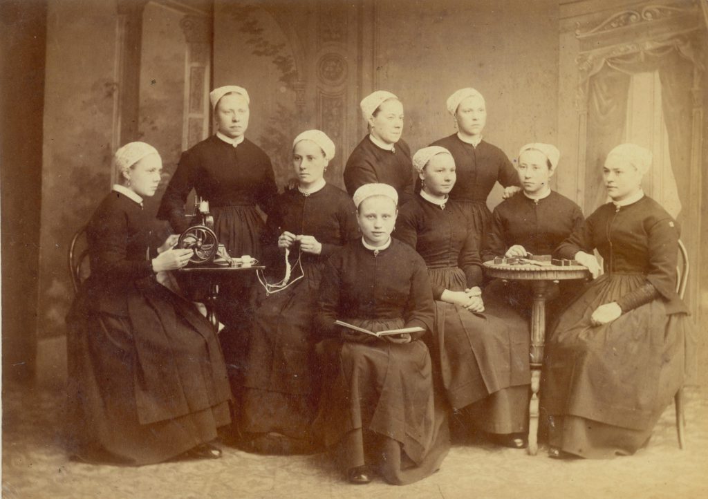 Weesmeisjes van het Weeshuis aan de Oude Delft, poserend in de naaikamer, ca. 1880, foto Emma Kirchner (TMS 1927)